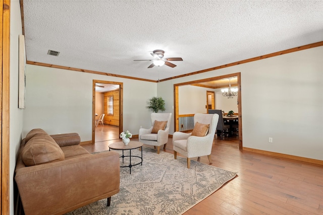 living room with hardwood / wood-style flooring, ceiling fan with notable chandelier, crown molding, and a textured ceiling