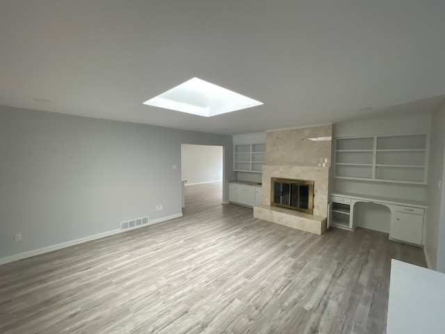 unfurnished living room with a skylight, light wood-type flooring, built in features, and a large fireplace