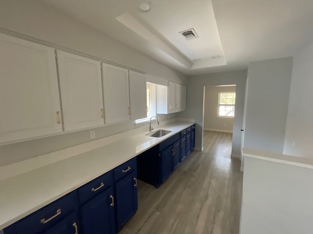 kitchen with blue cabinets, white cabinets, a raised ceiling, sink, and light hardwood / wood-style floors