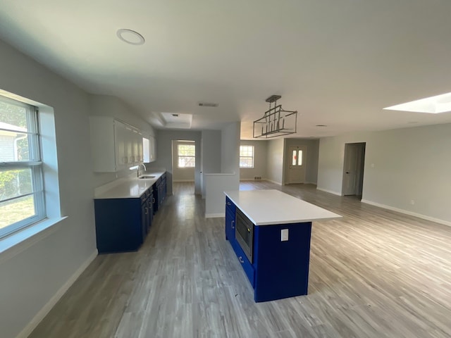 kitchen with blue cabinets, sink, light hardwood / wood-style flooring, white cabinetry, and stainless steel microwave