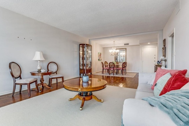 living area featuring a chandelier, wood finished floors, a textured ceiling, and visible vents