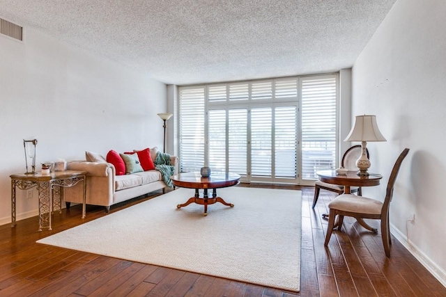 living room featuring a textured ceiling, baseboards, visible vents, a wall of windows, and hardwood / wood-style flooring