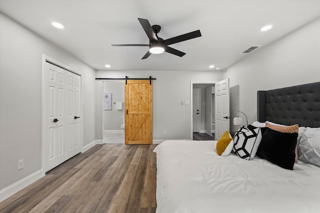 bedroom with a barn door, a closet, hardwood / wood-style flooring, and ceiling fan