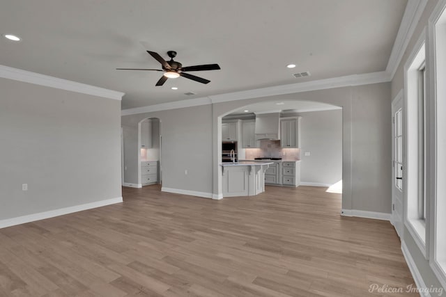 unfurnished living room with ceiling fan, ornamental molding, and light wood-type flooring