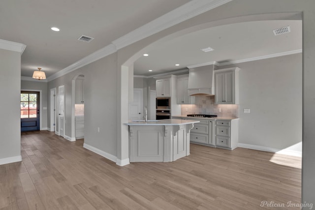 kitchen featuring light wood-type flooring, custom range hood, an island with sink, and appliances with stainless steel finishes