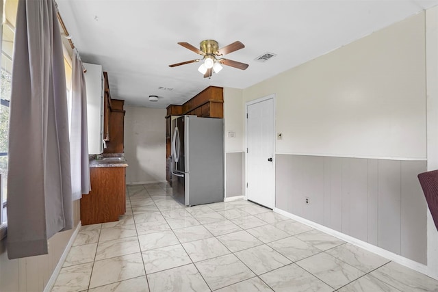 interior space with ceiling fan, wood walls, and stainless steel refrigerator