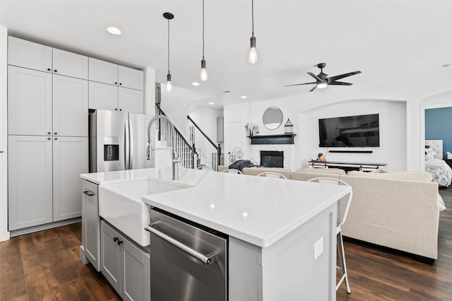 kitchen featuring a center island with sink, dark wood-type flooring, decorative light fixtures, and stainless steel appliances