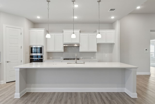 kitchen with light hardwood / wood-style floors, a spacious island, hanging light fixtures, and appliances with stainless steel finishes