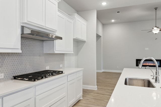 kitchen with stainless steel gas stovetop, white cabinets, sink, ceiling fan, and light wood-type flooring