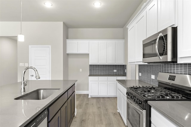 kitchen with stainless steel appliances, dark stone countertops, sink, decorative light fixtures, and white cabinetry