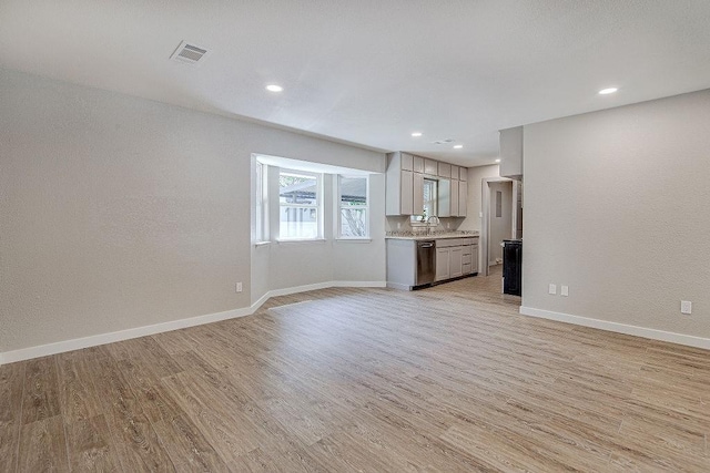 unfurnished living room featuring a sink, light wood finished floors, baseboards, visible vents, and recessed lighting