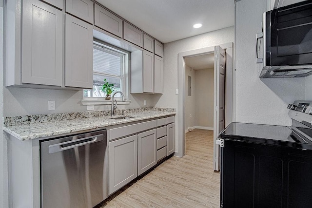 kitchen with gray cabinets, a sink, light wood-type flooring, light stone countertops, and appliances with stainless steel finishes