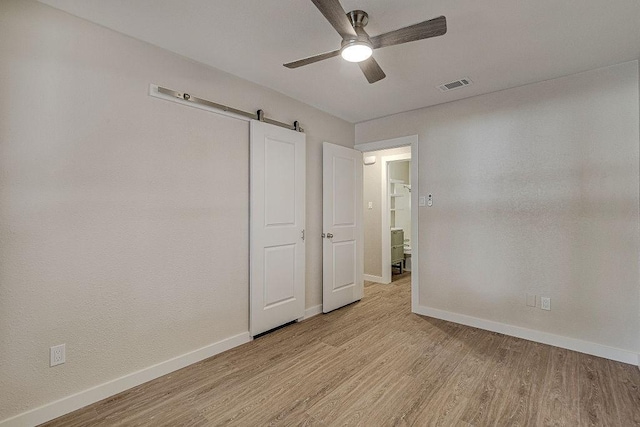 unfurnished bedroom featuring a barn door, visible vents, light wood finished floors, and baseboards