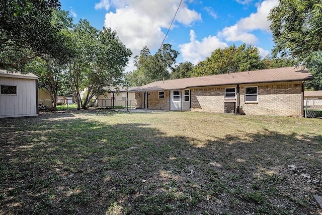 back of house with brick siding, a yard, an outbuilding, and fence