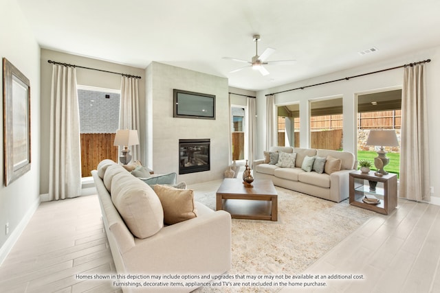 living room featuring light hardwood / wood-style floors, a tiled fireplace, and ceiling fan