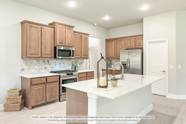 kitchen with sink, a center island with sink, stainless steel appliances, light wood-type flooring, and decorative backsplash