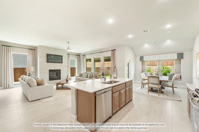 kitchen with sink, stainless steel dishwasher, light hardwood / wood-style flooring, a center island with sink, and a fireplace