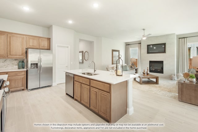 kitchen featuring a healthy amount of sunlight, a large fireplace, sink, stainless steel appliances, and an island with sink