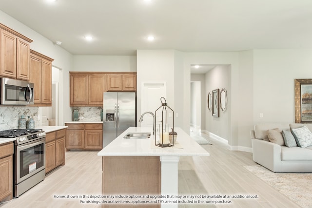 kitchen with an island with sink, stainless steel appliances, tasteful backsplash, sink, and light hardwood / wood-style floors