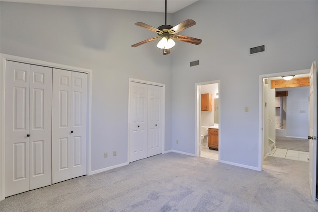 unfurnished bedroom featuring ensuite bath, multiple closets, high vaulted ceiling, and light carpet