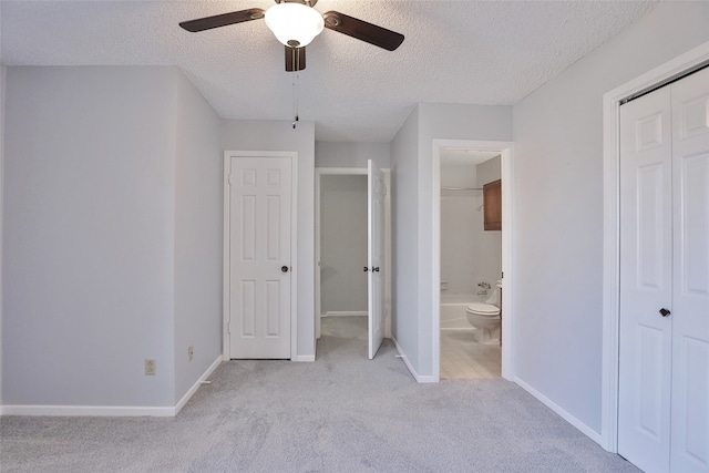 unfurnished bedroom featuring ensuite bathroom, ceiling fan, a textured ceiling, and light carpet