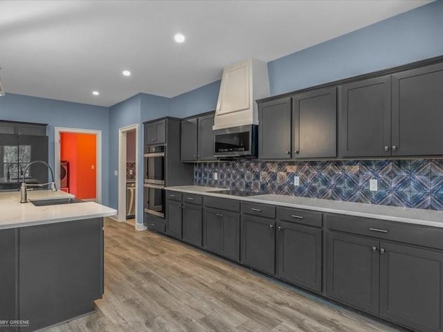 kitchen with sink, light hardwood / wood-style floors, decorative backsplash, and appliances with stainless steel finishes