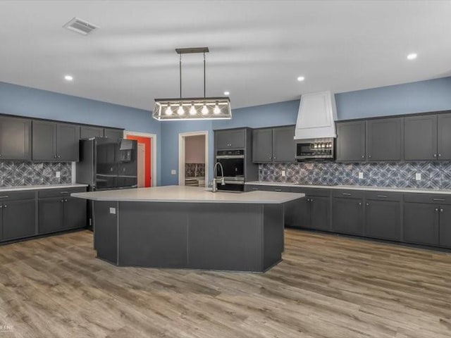 kitchen featuring black appliances, tasteful backsplash, hanging light fixtures, a kitchen island with sink, and gray cabinets