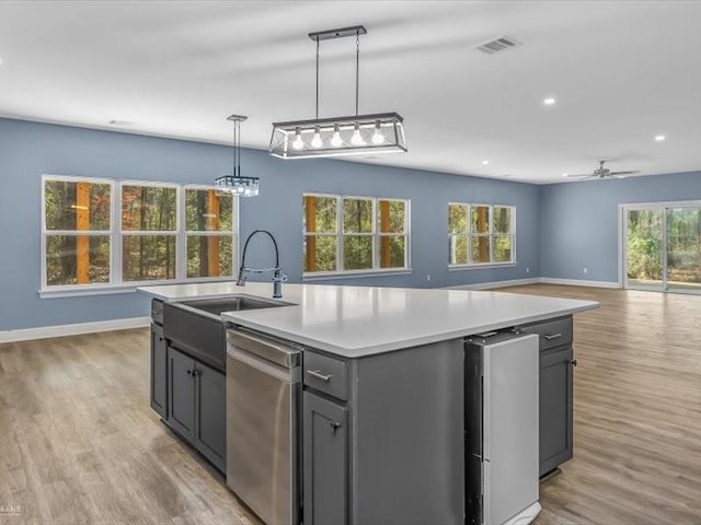 kitchen featuring sink, dishwasher, decorative light fixtures, and an island with sink