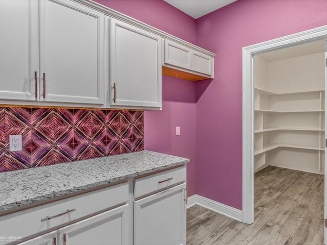 kitchen with light stone counters, light hardwood / wood-style floors, backsplash, and white cabinets