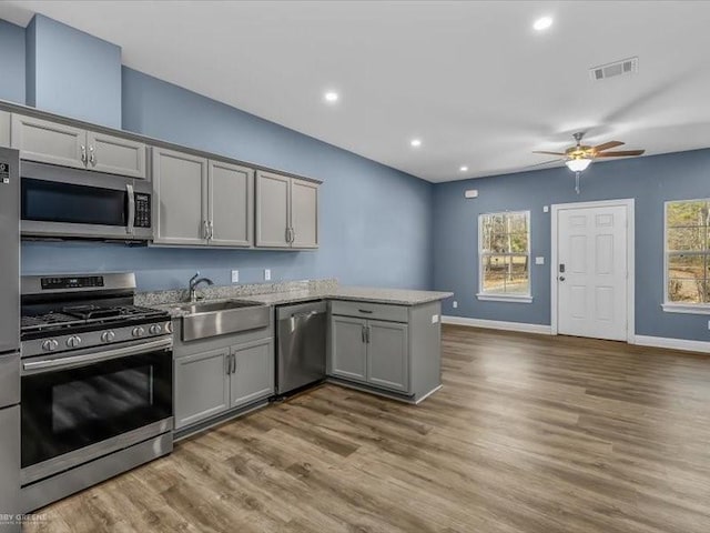 kitchen with kitchen peninsula, sink, hardwood / wood-style flooring, gray cabinets, and stainless steel appliances