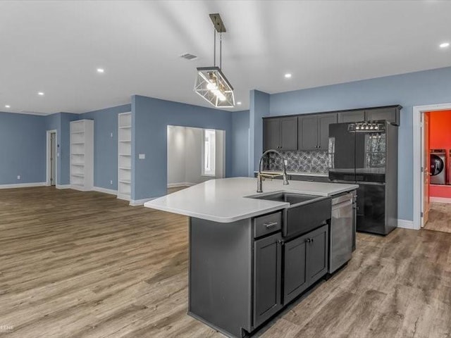 kitchen with tasteful backsplash, a kitchen island with sink, stainless steel dishwasher, gray cabinetry, and washer and clothes dryer