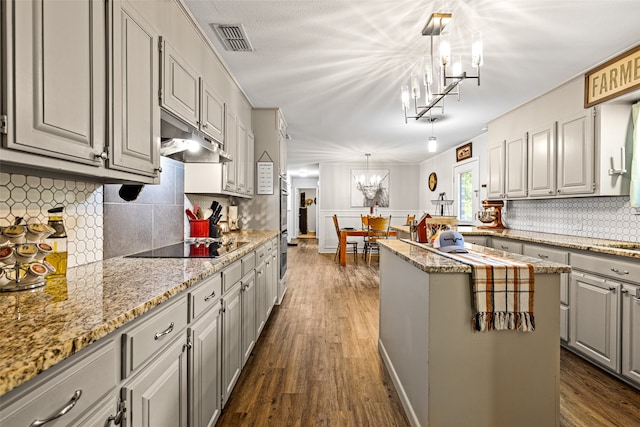 kitchen with tasteful backsplash, hanging light fixtures, a kitchen island, black electric cooktop, and dark hardwood / wood-style floors