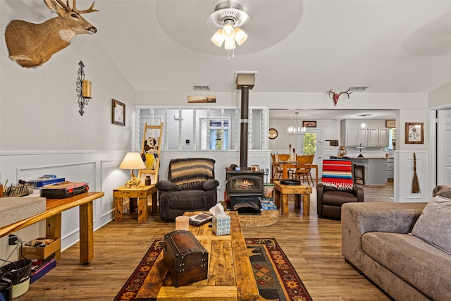 living room featuring light hardwood / wood-style floors, a wood stove, lofted ceiling, and ceiling fan with notable chandelier