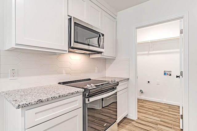 kitchen with light wood-type flooring, light stone counters, stainless steel appliances, tasteful backsplash, and white cabinetry