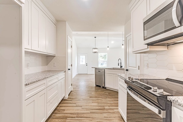 kitchen featuring hanging light fixtures, white cabinetry, appliances with stainless steel finishes, light hardwood / wood-style floors, and decorative backsplash