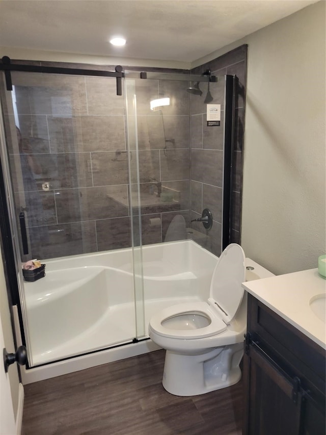 bathroom with a shower with door, hardwood / wood-style floors, vanity, and toilet