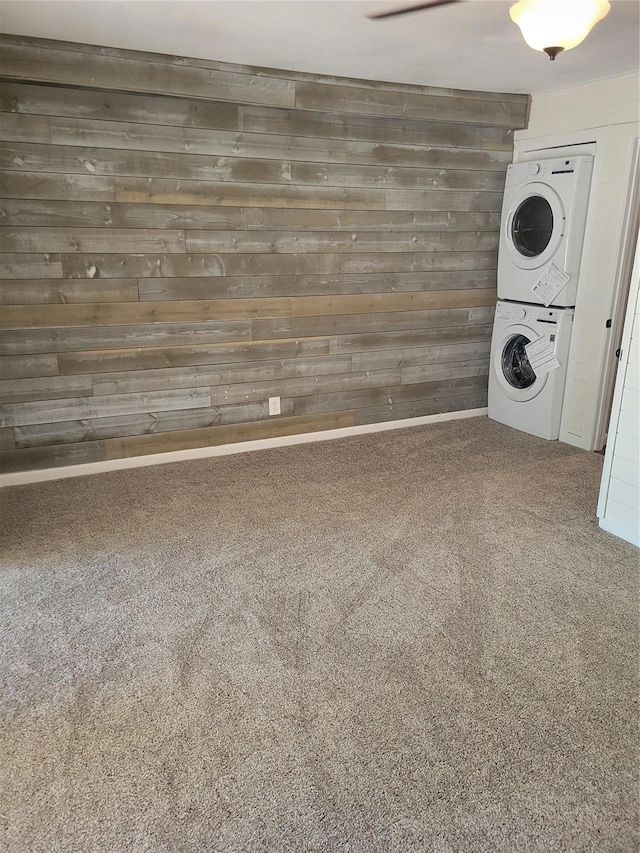 laundry area featuring carpet floors, stacked washer and dryer, wooden walls, and ceiling fan