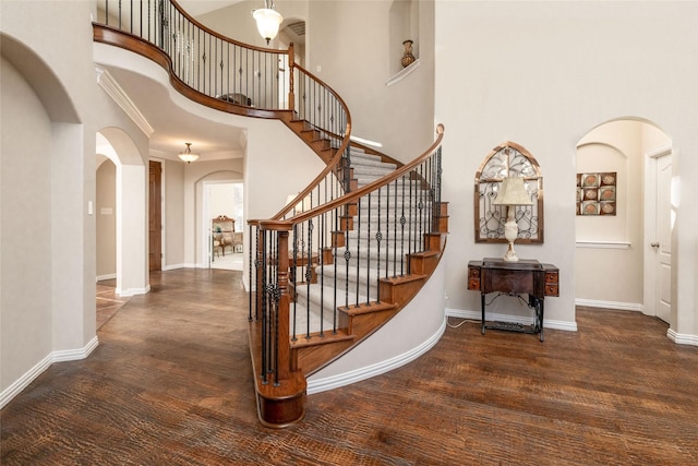 stairway with arched walkways, wood finished floors, and baseboards