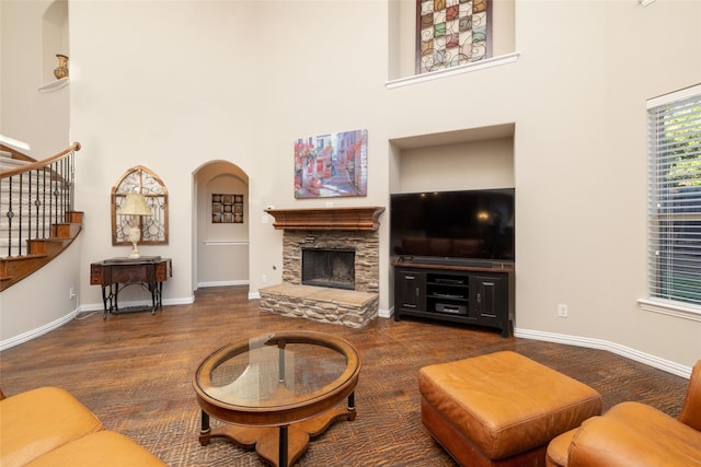 living room with a stone fireplace, a towering ceiling, and dark wood-type flooring