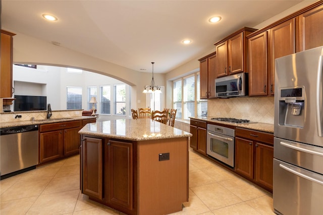 kitchen featuring appliances with stainless steel finishes, a center island, light stone counters, and hanging light fixtures