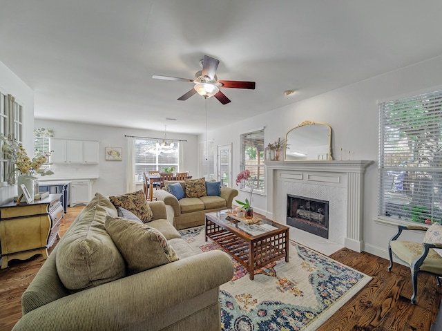 living room with ceiling fan with notable chandelier, hardwood / wood-style flooring, and a tiled fireplace