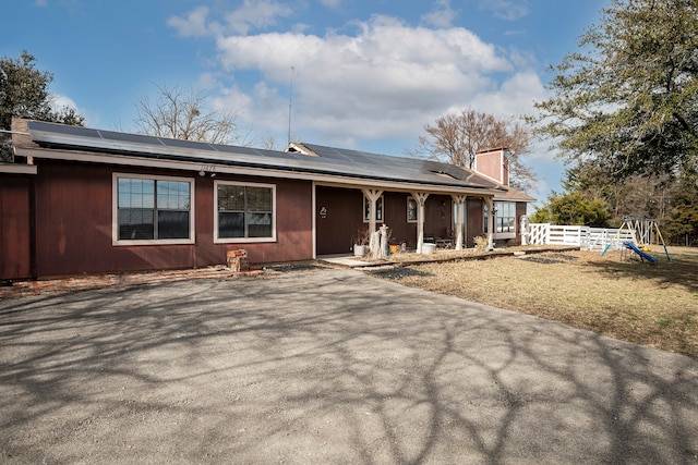 single story home featuring a front yard, solar panels, a playground, and covered porch