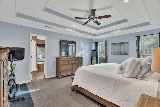 carpeted bedroom featuring ceiling fan, ensuite bathroom, and a tray ceiling