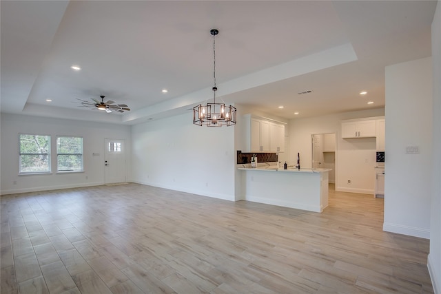 interior space with light wood-type flooring, pendant lighting, white cabinetry, and a raised ceiling