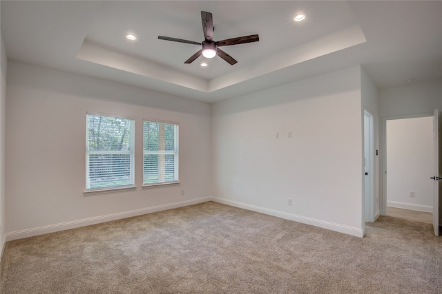 carpeted empty room with ceiling fan and a tray ceiling