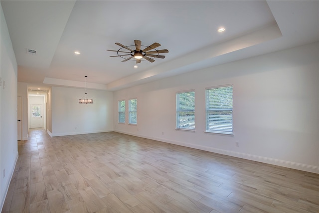 spare room featuring ceiling fan with notable chandelier, a tray ceiling, and light hardwood / wood-style flooring