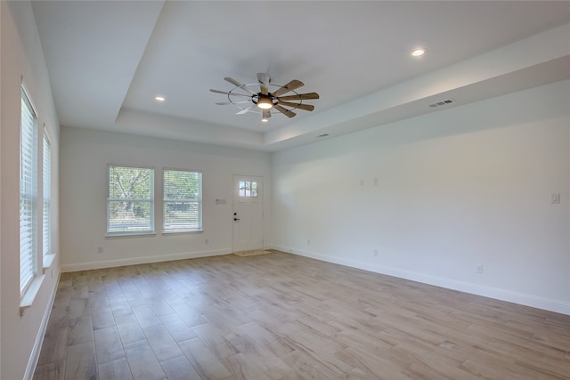 unfurnished room with ceiling fan, a tray ceiling, and light hardwood / wood-style flooring