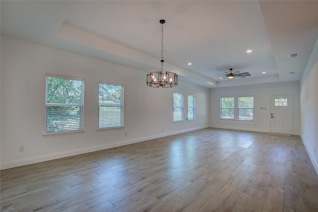 unfurnished room featuring ceiling fan with notable chandelier, a raised ceiling, and light hardwood / wood-style floors