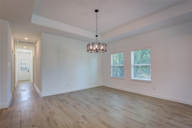 spare room featuring a notable chandelier, a tray ceiling, and light hardwood / wood-style floors