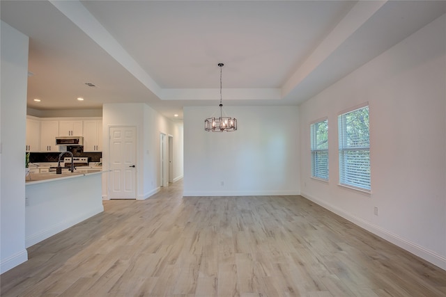 interior space with light wood-type flooring, a tray ceiling, sink, and an inviting chandelier